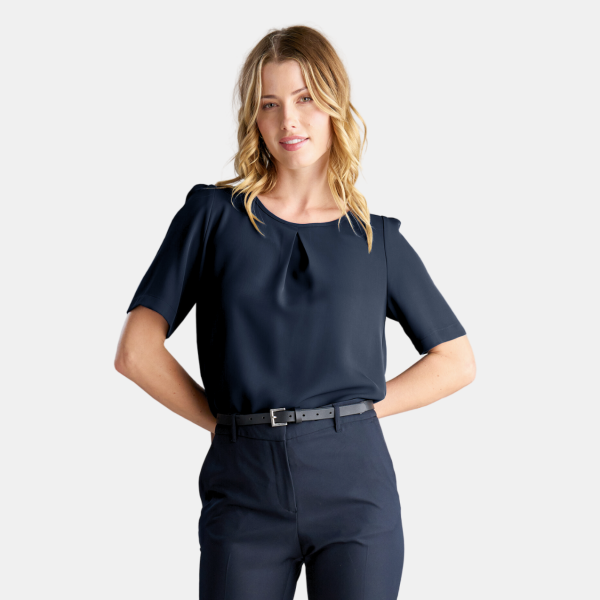 a Woman Posing with Her Hands on Her Hips, Showcasing the Short-sleeved Navy Blouse. the Blouse Features a Pleat Detail at the Front of the Blouse and is Tucked into Navy Trousers, Which Are Accented with a Black Belt, Highlighting the Waist. the Attire Maintains a Professional Business-casual Aesthetic.