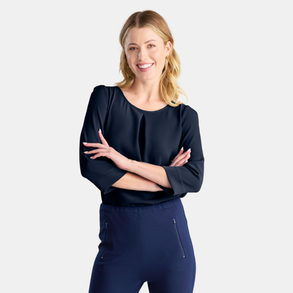 a Woman is Standing Posing for the Camera, Arms Folded Confidently Across Her Chest, Wearing a 3/4 Sleeve Navy Blouse. the Blouse Features a Subtle Pleat at the Front, Giving It a Touch of Elegance. the Sleeves Are Cuffed for a Smart Finish. She is Paired with Matching Navy Trousers That Are Fitted with a Black Belt to Cinch at the Waist. the Outfit Suggests a Professional, Business-casual Look.