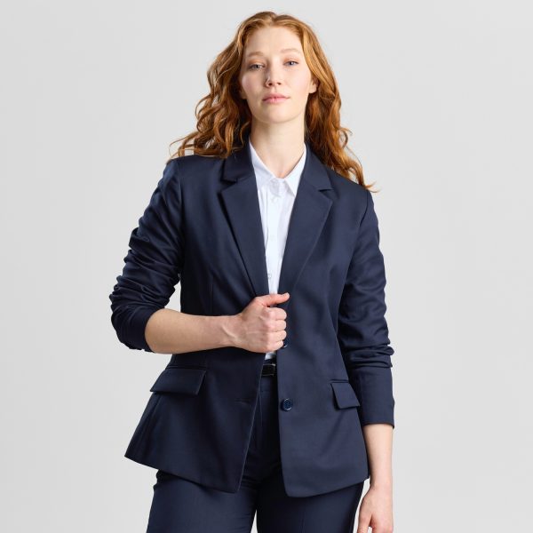 Woman Wearing a French Navy Classic 2-button Blazer, Slightly Open to Reveal a White Shirt, Posing with One Hand Buttoning the Blazer.