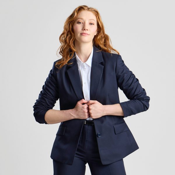 Front View of a Woman Buttoning a French Navy Classic 2-button Blazer over a White Shirt, with a Soft Smile on Her Face.