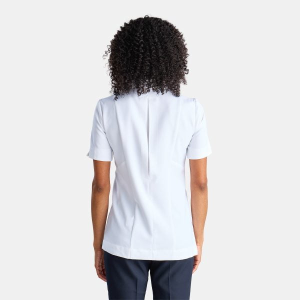 Back View of a Woman Wearing a White Asymmetric Pharmacy Jacket with Short Sleeves, Paired with Navy Pants.