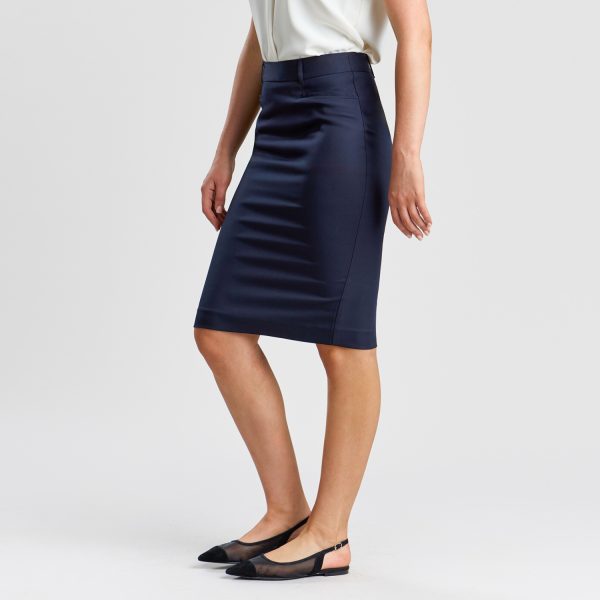 Side Angle View of a Person in a French Navy Classic Pencil Skirt and White Blouse, with Hands Gently Touching the Skirt, Paired with Black Ballet Flats on a White Backdrop.