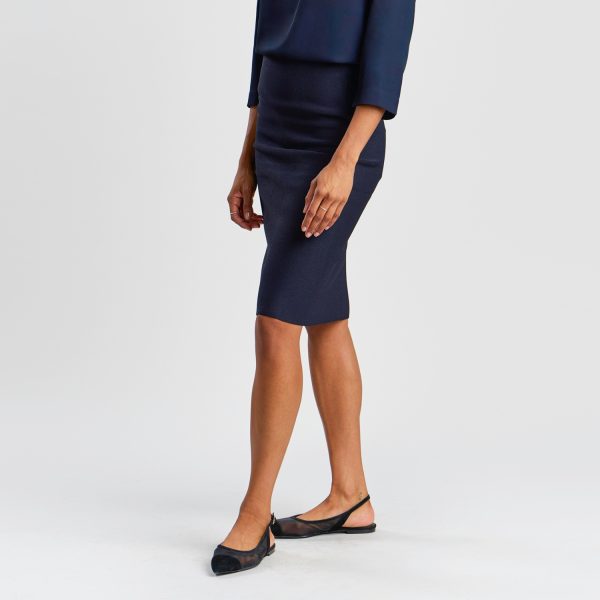 a Woman Modelling a French Navy Milano Knit Pencil Skirt and Black Flats Against a White Background.