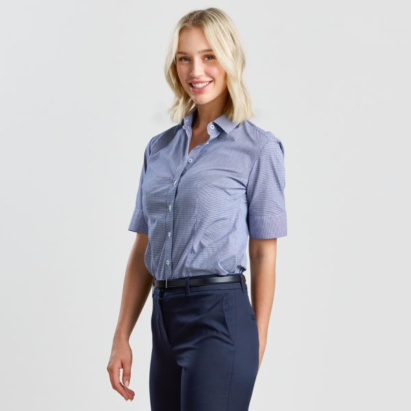 a Woman with a Pleasant Smile Wearing a Navy Mini Check Short Sleeve Shirt, Partially Turned to Display the Shirt's Fit and Check Pattern.
