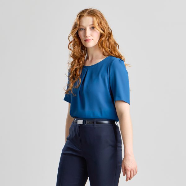 Woman Wearing a Blue Centre Pleat Blouse with Short Sleeves and Navy Trousers, Standing with a Neutral Expression.