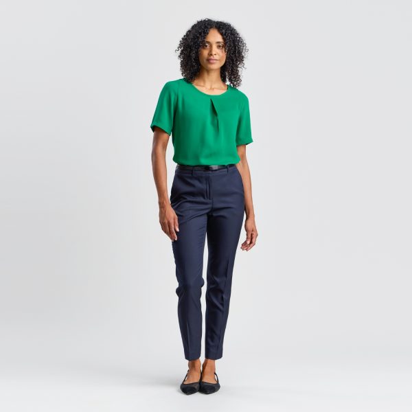 a Model Poses in a Tailored Emerald Green Blouse with Center Pleat and Navy Trousers Against a Neutral Backdrop.