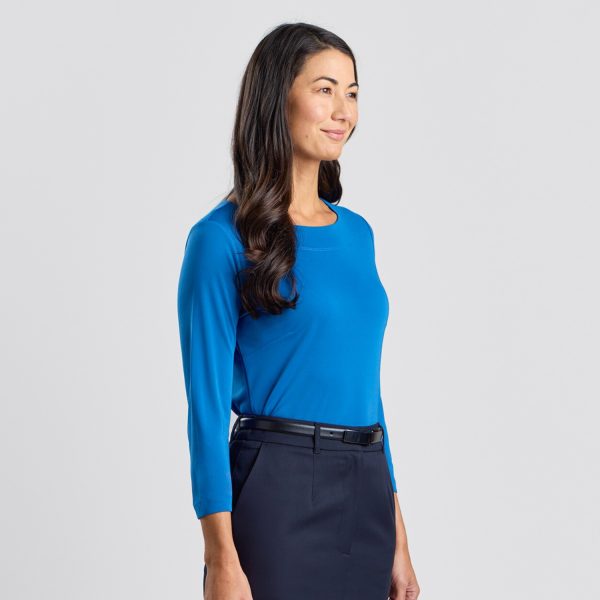 a Side Angle of a Woman Smiling Gently, Wearing a Marine Blue Soft Knit 3/4 Sleeve Boat Neck Top with a Navy Skirt Against a White Background.