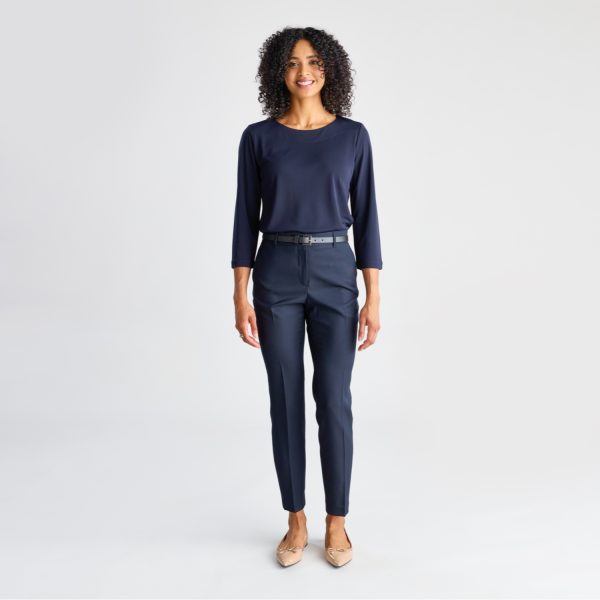 Full-length Image of a Cheerful Woman Wearing a Navy Soft Knit 3/4 Sleeve Boat Neck Top with Coordinating Trousers and Beige Heels, Posing Against a White Backdrop.