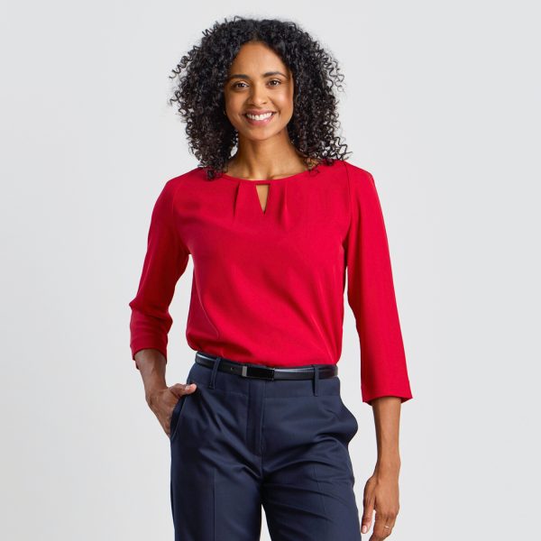 the Model Smiles, Hands on Hips, in a Ruby Blouse with Keyhole Neckline, Paired with Navy Trousers.