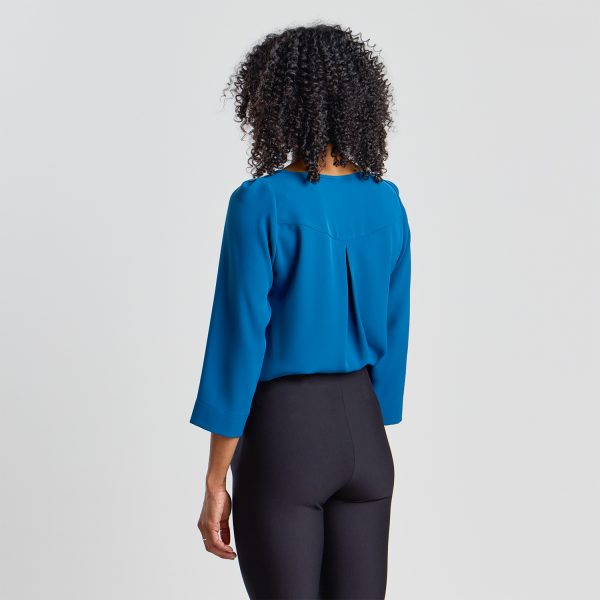 Back View of a Woman with Curly Hair Wearing a Blue 3/4 Sleeve Blouse and Black Trousers.