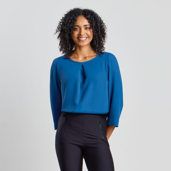 Front View of a Smiling Woman with Curly Hair Wearing a Blue 3/4 Sleeve Blouse and Black Trousers."