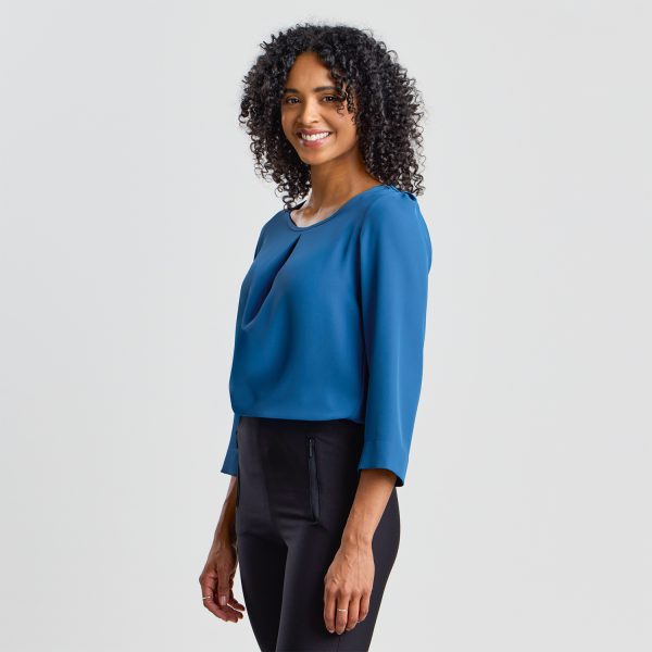 Side View of a Smiling Woman with Curly Hair Wearing a Blue 3/4 Sleeve Blouse and Black Trousers.