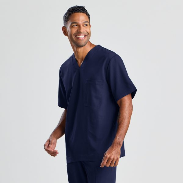 Angled View of a Man Smiling and Confidently Modeling the Men's Modern Scrub Top in Navy, Showcasing a V-neck and Chest Pocket Design.