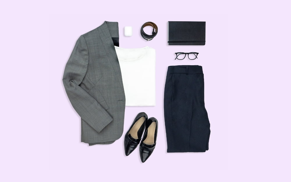 The banner for the article 'How to Measure Yourself for the Perfect Fit' features a flat lay of corporate-style garments and an assortment of accessories that a corporate worker may wear and use at work. The items lay atop a light purple background.