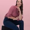 the Banner for the Article 'the Real Roi of Work Uniforms' Depicts a Professional-looking Female Wearing a Pink Linen, Button-up Blouse and Navy Slacks Manufactured by Designs to You. She is Sitting Atop a Black Chair and Smiling Radiantly at the Camera in Front of a Pink Background.