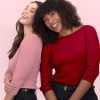 the Banner for the Article 'giving Your Uniforms a Unique (and Colourful) Edge' Depicts Two Female Models Leaning Against Each Other Looking Happy, Confident and Smiling for the Camera. They Stand in Front of a Baby Pink Background and Are Wearing Colourful and Coordinating Milano Knit Boat Neck Tops with 3/4 Sleeves Manufactured by Designs to You.
