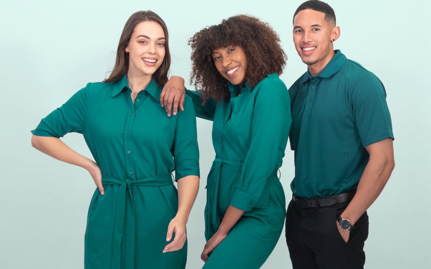 The banner for the article 'Creating a Killer Uniform for Your Team' depicts two female and one male model posing together in front of a pale mint background. They are each smiling for the camera and wearing coordinating teal coloured uniforms manufactured by Designs To You. Together, they look professional, confident and stylish.