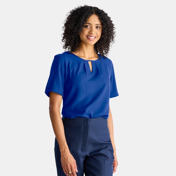 a Smiling Woman in a Professional Short Sleeve Blue Top. the Keyhole Blouse is Comfortable and Stylish, Paired with a Pair of Navy Work Pants