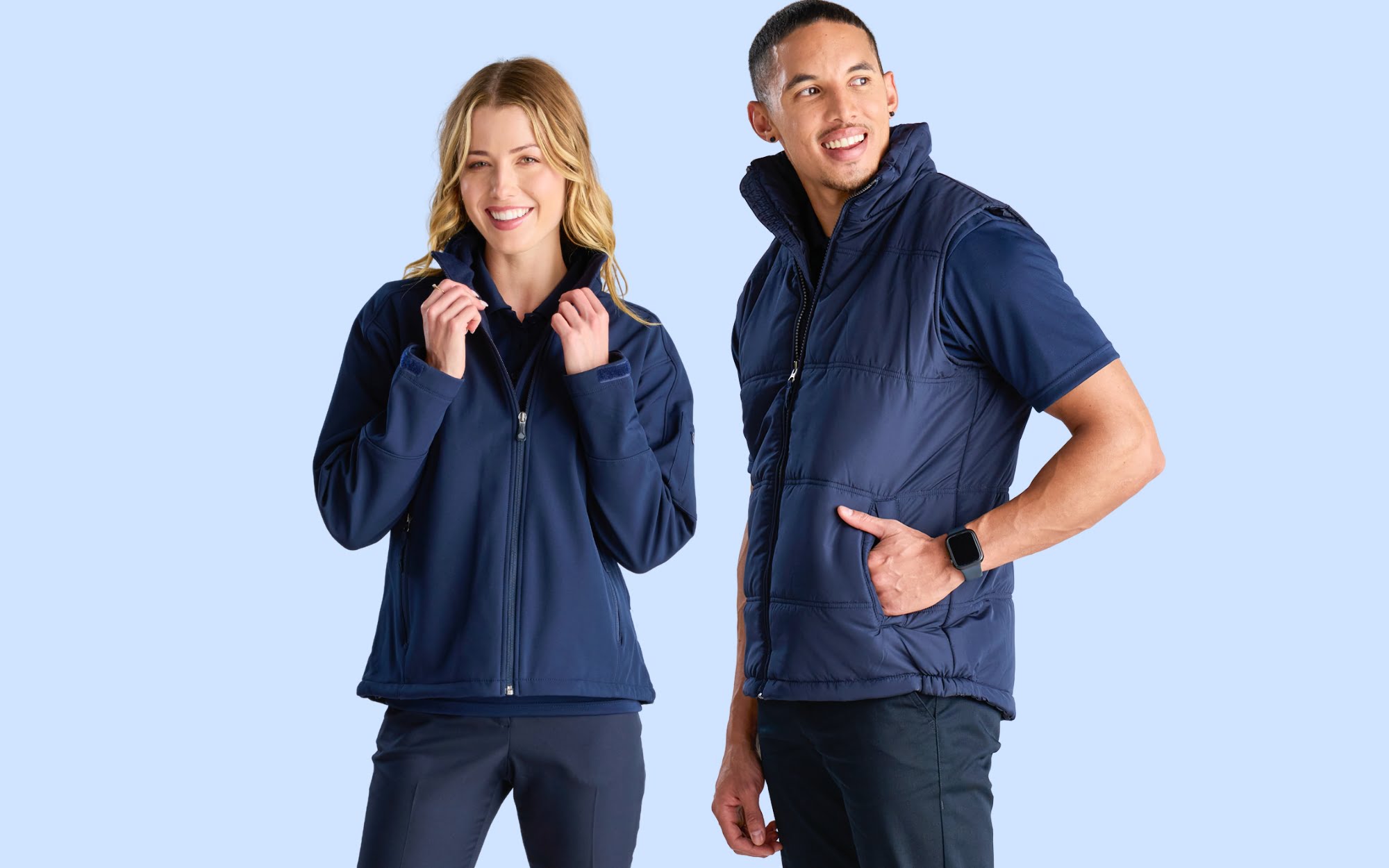 The banner for the article 'Uniforms Without an A-Gender' displays a blue background. In the foreground, a male and female model stand side by side, both wearing unisex jackets. The jackets are designed to be gender-neutral, emphasising inclusivity and breaking traditional gender norms in uniform attire. The blue background adds a visually appealing and modern touch to the banner, drawing attention to the article's exploration of gender-neutral uniforms.