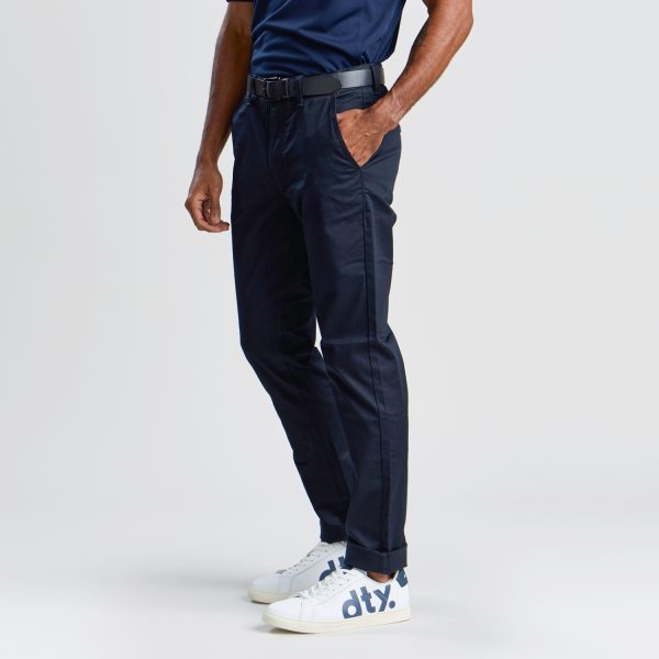 Side Profile of Men's Slim Style Chino Pant in French Navy, Featuring a Sleek Fit with a Rolled Cuff, Worn with a Dark Polo Shirt and White Branded Sneakers.