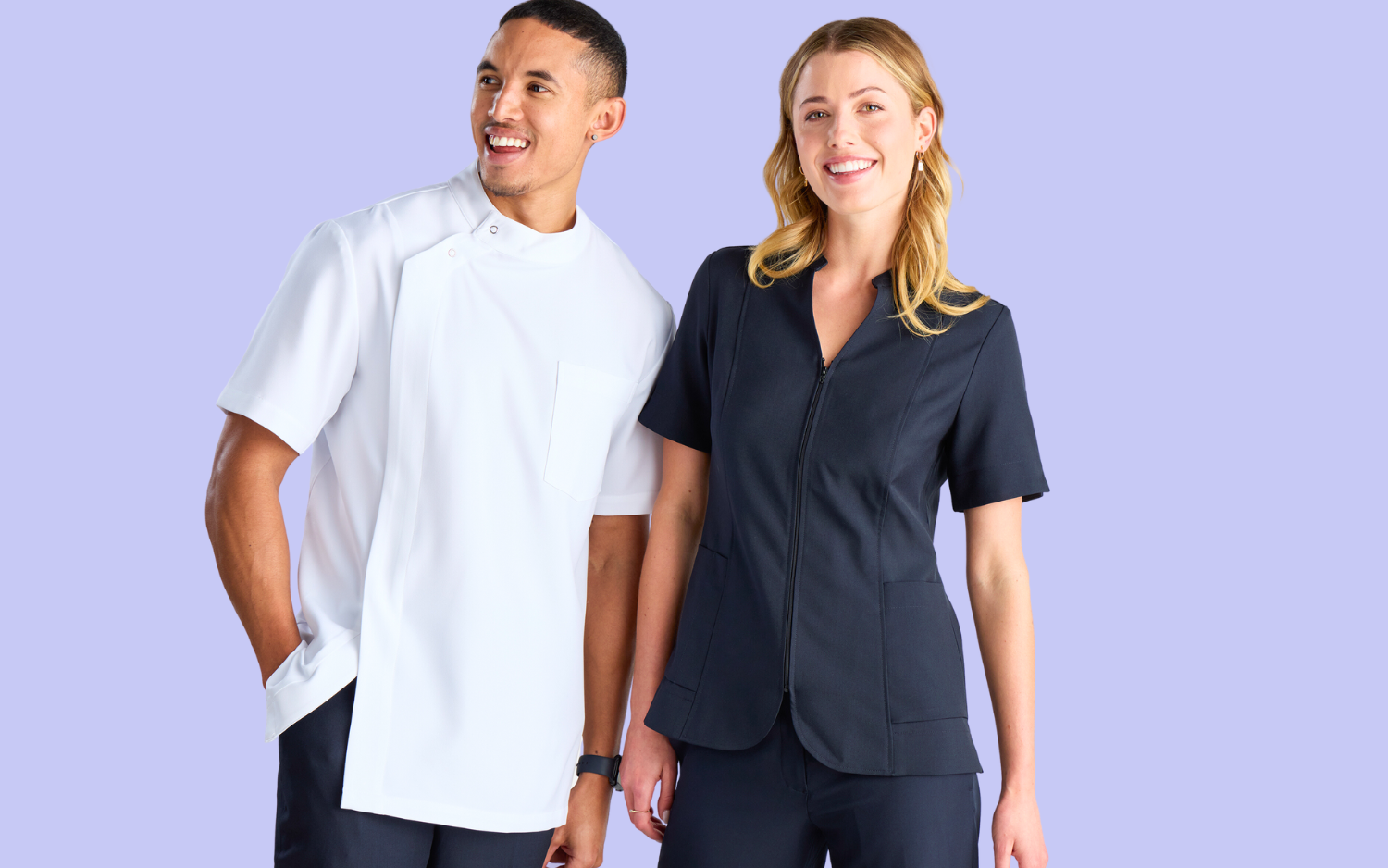 Pharmacy Uniforms Australia: A smiling young woman and man posing together. The man is wearing a classic pharmacy jacket, and the woman is wearing a french navy zip front tunic.