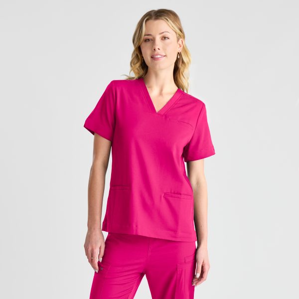 a Woman with Blonde Hair Stands Wearing a Fuchsia Pink Women's Modern Scrub Top with Matching Pants, Exuding a Professional and Vibrant Look Against a White Background.