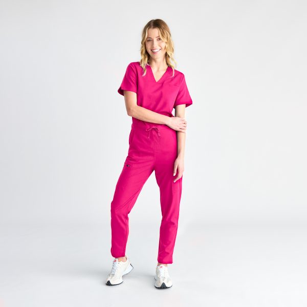 Full-body Image of a Smiling Woman Posing in a Fuchsia Pink Women's Modern Scrub Top and Pants, Complemented by White Sneakers for a Comfortable and Stylish Healthcare Outfit.
