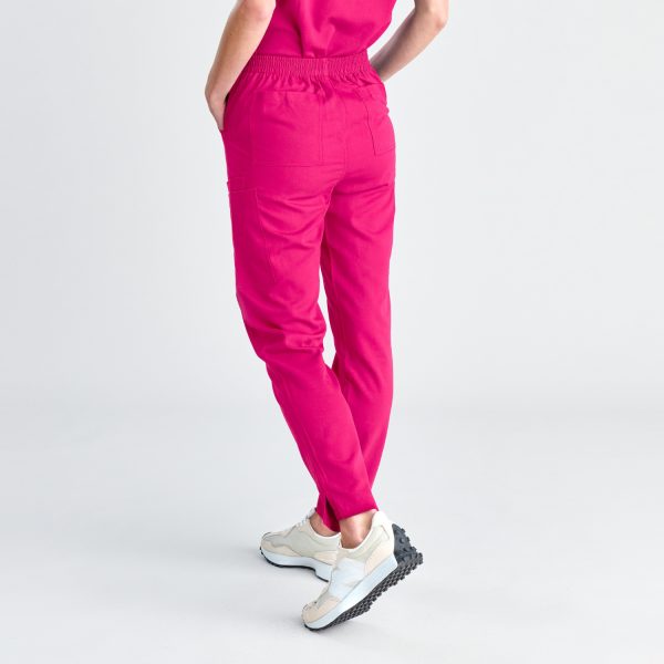 Rear View of a Woman Wearing Fuchsia Pink Women's Modern Scrub Pants Paired with White Sneakers, Showcasing the Fit and Pocket Detailing Against a White Background.