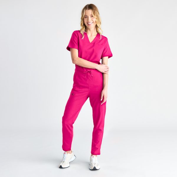 Full-length Image of a Woman Smiling in Fuchsia Pink Women's Modern Scrub Pants, Complete with a Casual Tucked-in V-neck Top and White Athletic Sneakers for a Sporty, Professional Look.
