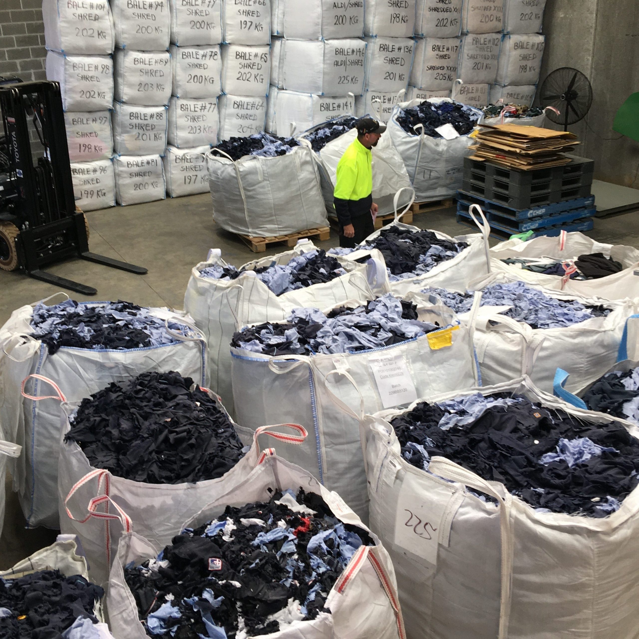 Sustainable Uniforms and Uniform Recycling - an image of inside a textile recycling warehouse. Old uniforms are pictured within bags awaiting recycling.