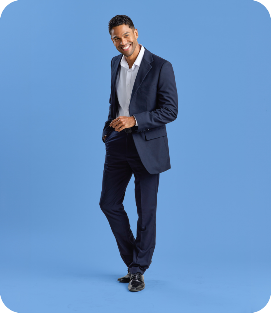 a Man in a Navy Suit with a White Shirt, Smiling and Posing with His Hands in His Pockets, Standing Against a Blue Background.