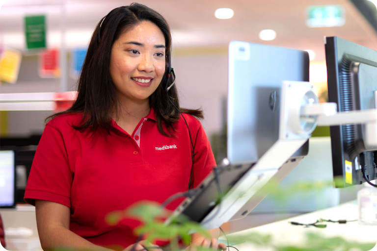 A Medibank employee, dressed in a red Medibank polo shirt, works at a computer while speaking through a headset, demonstrating the company's efficient customer service.