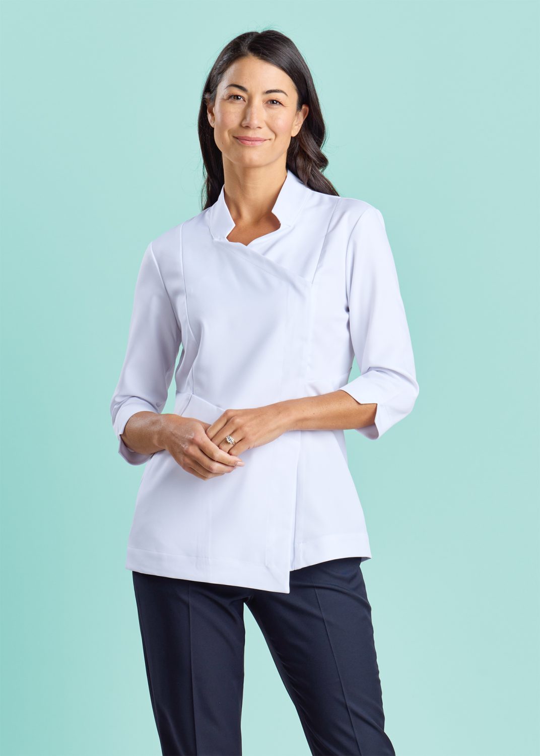 a Female Pharmacist Wearing a Crisp White Wrap-style Tunic with a Mandarin Collar and 3/4-length Sleeves, Standing Confidently Against a Soft Teal Background.