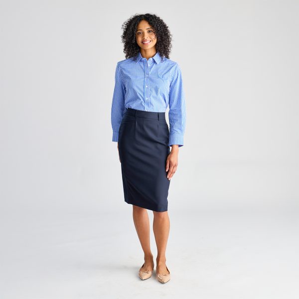 Full Body Shot of a Woman Standing, Dressed in a Blue Checkered Long Sleeve Shirt and a Navy Skirt with Beige Flats.