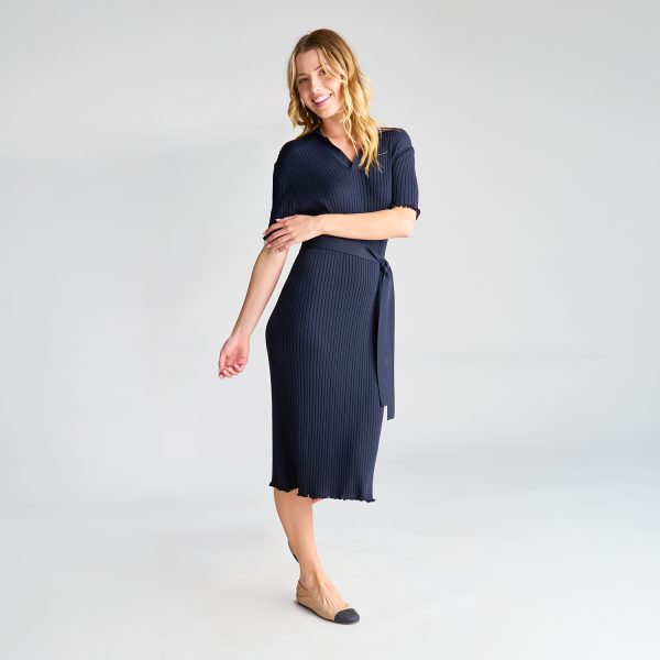 Woman Wearing a Navy Milano Knit Dress with a Tie Belt, Smiling and Standing Slightly Turned.