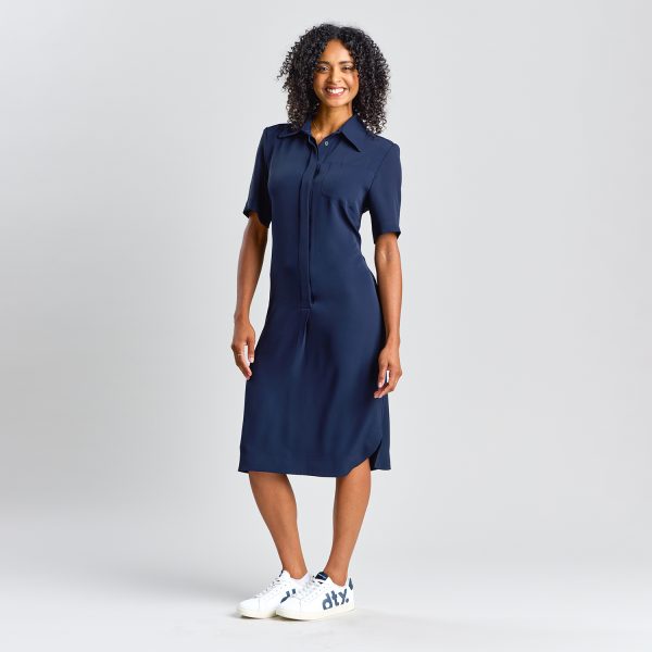 Woman Wearing a Short-sleeve, Button-up Navy Healthcare Shirt Dress with a Collar, Mid-length Hem, and Subtle Side Slits, Standing with Hands Relaxed by Side.