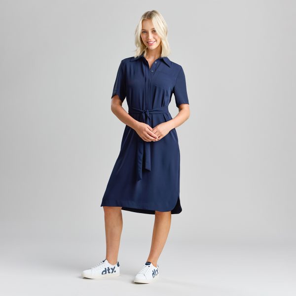 Woman Wearing a Navy Healthcare Shirt Dress with a Belt Tied Around the Waist, Smiling with Hands Resting at the Front.