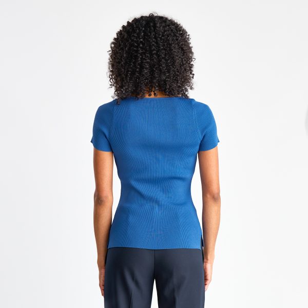 Back View of a Woman Wearing a Blue Short Sleeve Milano Knit Boat Neck Top Paired with Navy Pants.