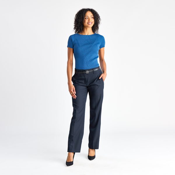 Full Length View of a Woman in a Blue Short Sleeve Milano Knit Boat Neck Top, Hands in Pockets, with Navy Trousers.