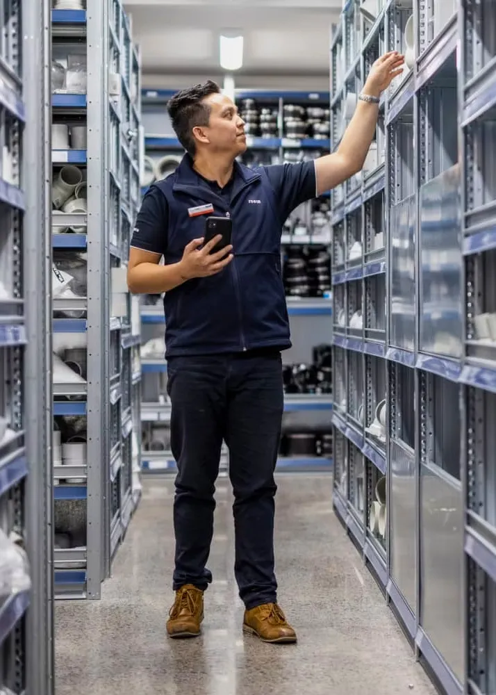 Reece employee in warehouse uniform reaching for stock, wearing gear designed to support movement and reduce strain during physical tasks.