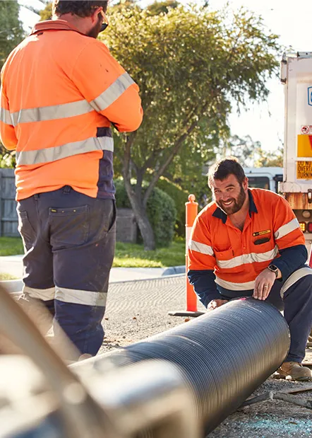 Two tradies in high-visibility workwear laying pipe on-site, demonstrating how work uniforms and injury prevention come together in real conditions.