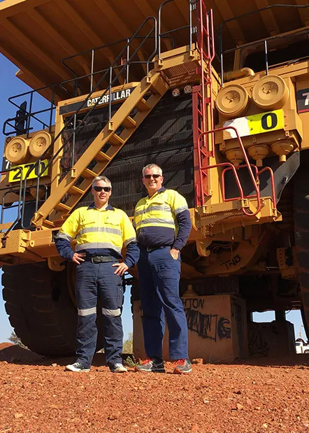 Two workers in high-visibility yellow work uniforms standing in front of a mining truck, showing how durable uniforms support safety and injury prevention on site.