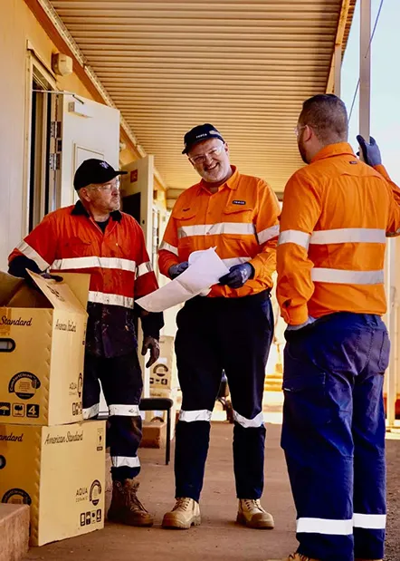 Three Reece workers in high-visibility orange uniforms reviewing site paperwork, showing how work uniforms and injury prevention support real-world teamwork.
