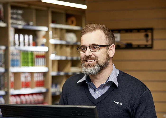 Reece team member in branded retail uniform behind the counter, showing professional workwear built for comfort, branding, and mobility.